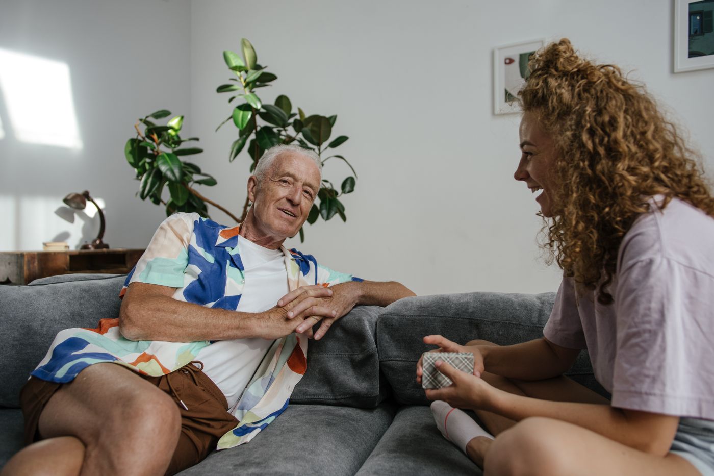 A grandfather and his adult granddaughter talking warmly together on a sofa — generations having the conversation with respect