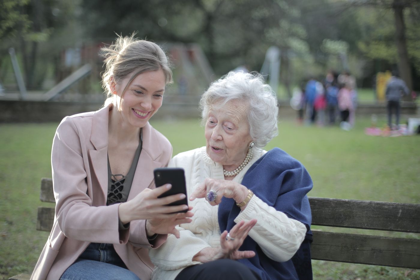 An adult daughter showing her smiling elderly mother something on a smartphone — the start of a calm, dignity-first conversation